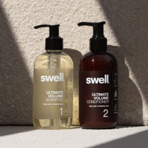 A pack shot of Swell volume shampoo and volume conditioner on a light stone background