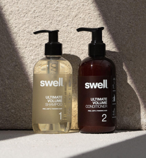 A pack shot of Swell volume shampoo and volume conditioner on a light stone background